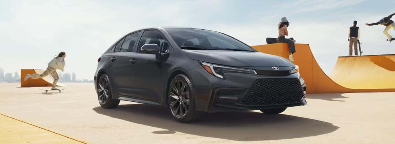 Front three-quarter view of a gray Toyota Corolla parked at a skaepark on a sunny day.