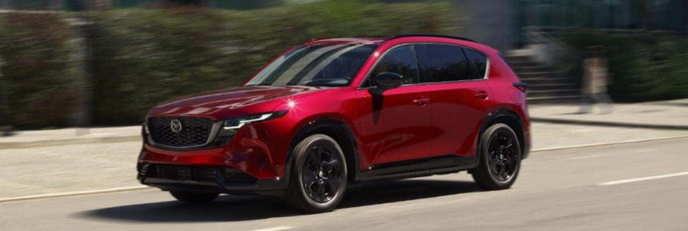 Exterior side view action shot of a red Mazda CX-5 driving down a city street.