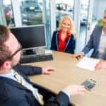 Couple buying car at dealership and negotiating price with salesman