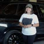 Daffne Gaitan standing in front of a black polished BMW X5 inside of a garage.