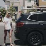 Brecht family walking in beach clothes to their new BMW X3 in black with surfboards on their rack.