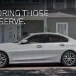 BMW 3 Series Sedan, white in color and in front of an older home.