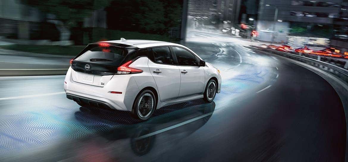 A white 2025 Nissan Leaf driving down a bridge in a city