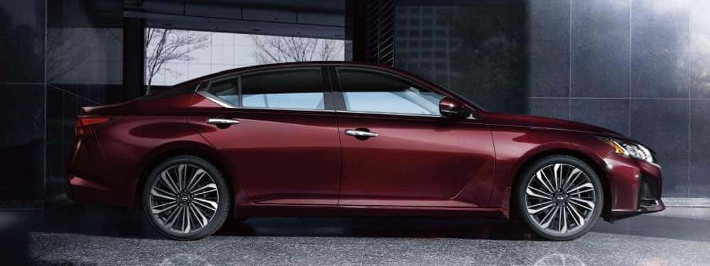 A red Nissan Altima in profile, parked next to a building