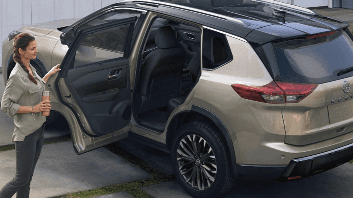A light-colored Nissan Rogue parked in a driveway with a family getting inside