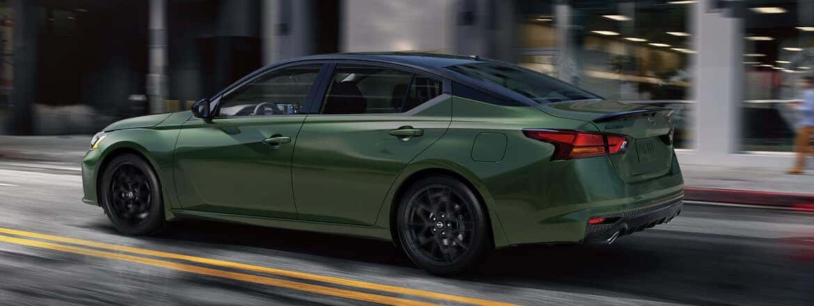 A green Nissan Altima driving down the road