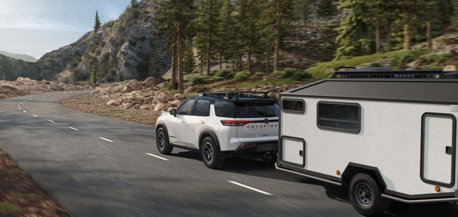 A white Nissan Pathfinder towing a trailer while driving path a forest