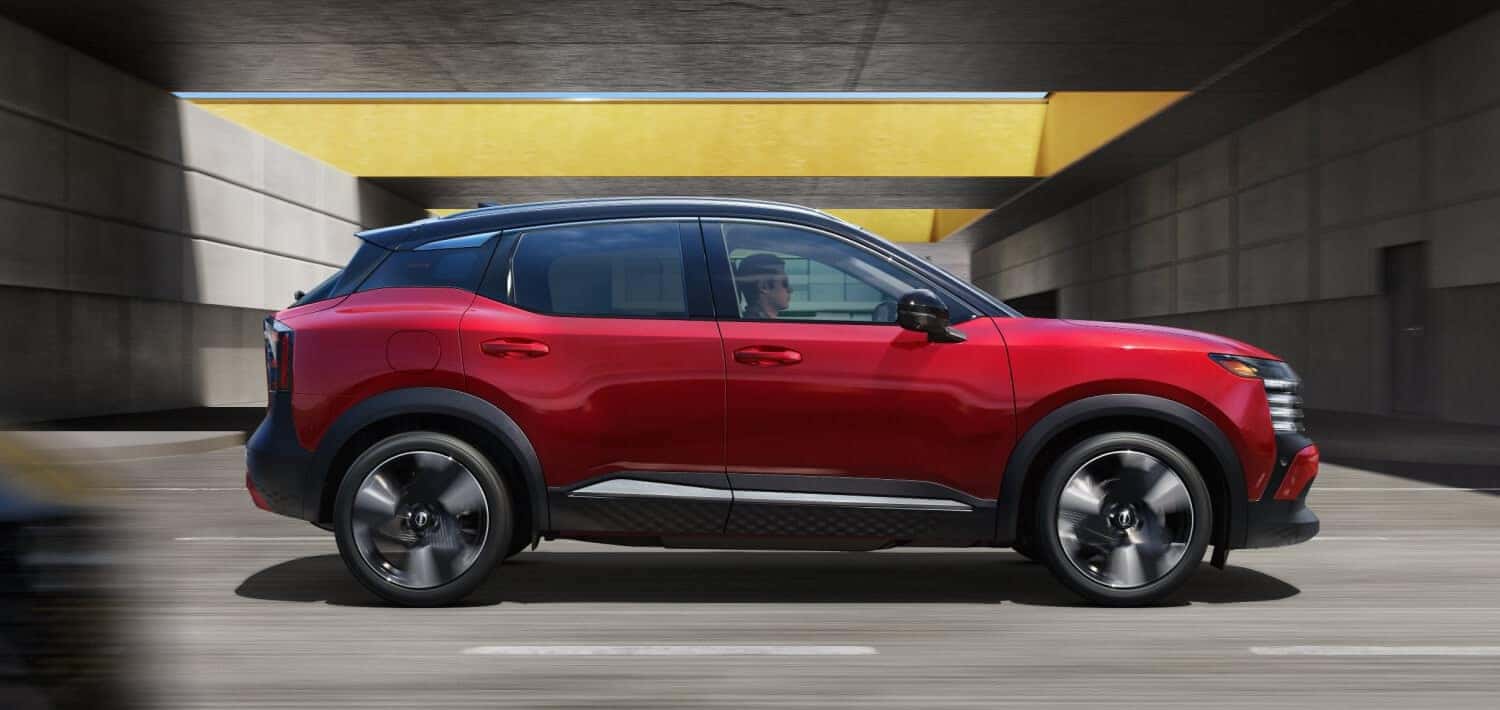 A red Nissan Kicks in profile driving down the road