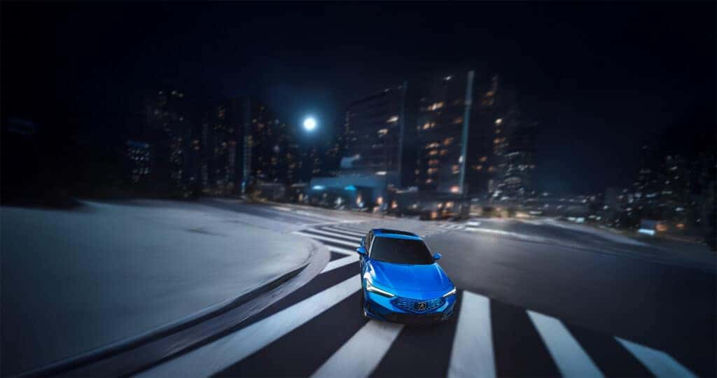 A Double Apex Blue Pearl colored 2026 Acura Integra A-Spec driving around a corner in a city at night