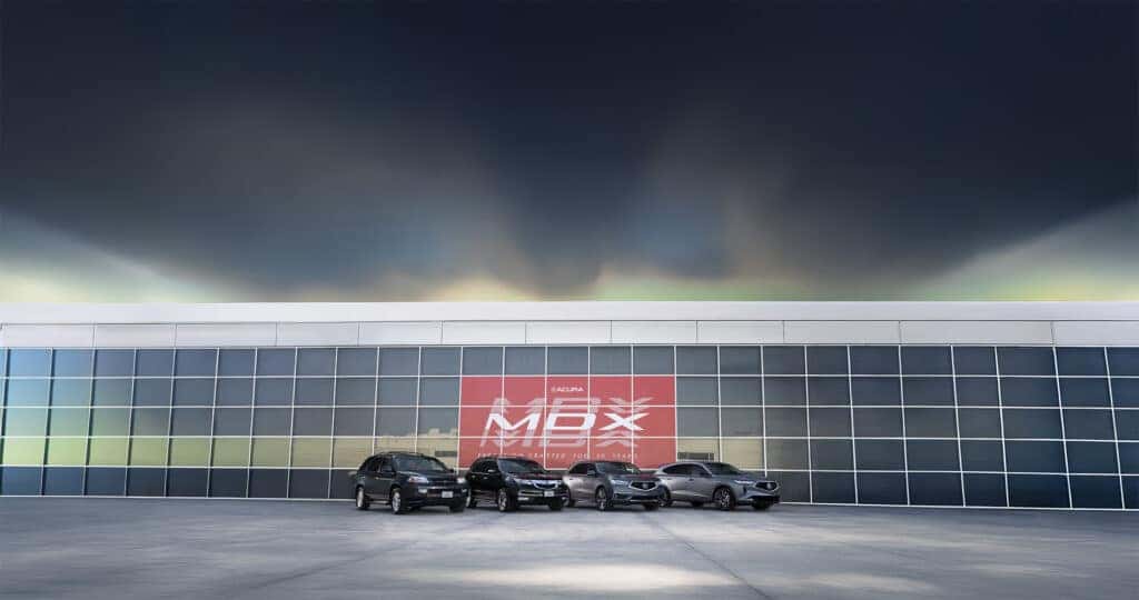 All Acura MDX Generations Parked In Front of a Large Glass Building