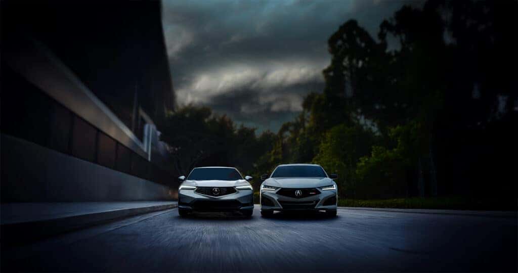 A 2026 Acura Integra vs TLX driving down a city street with dark storm clouds above