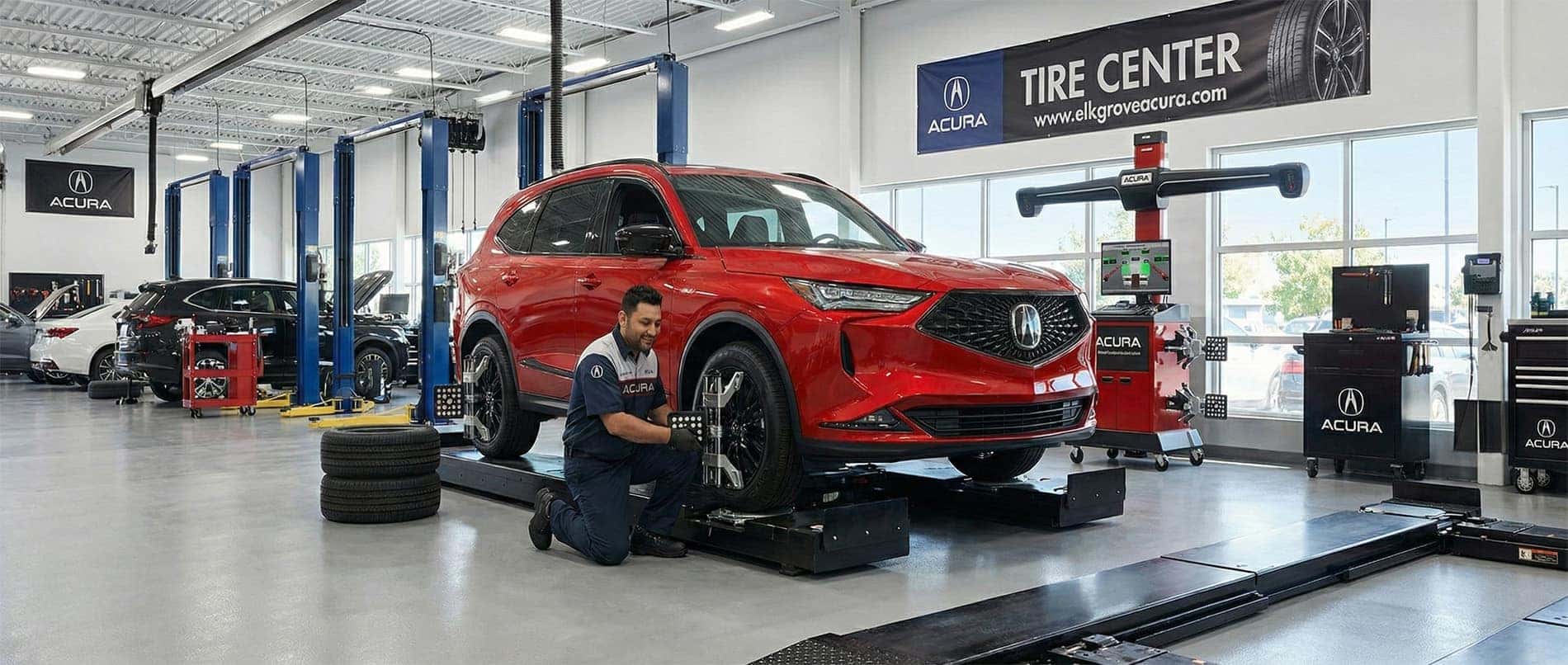 A red Acura MDX SUV in an Acura tire center replacing tires on an alignment rack