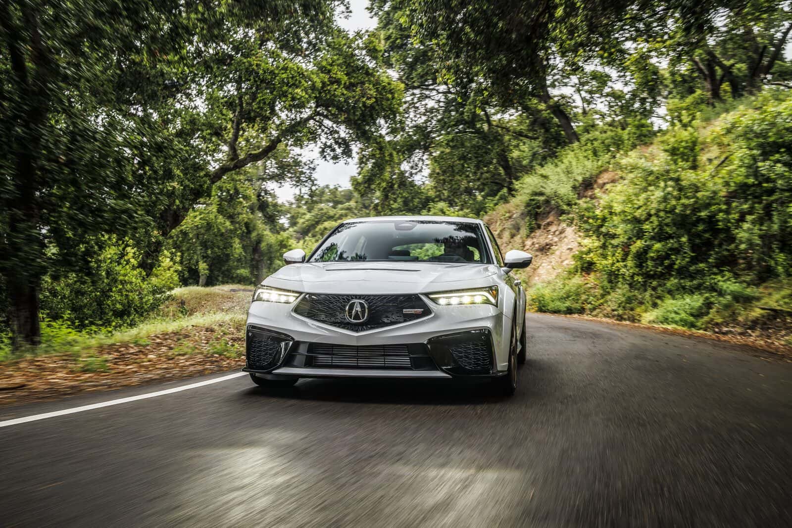 2026 Acura Integra Type S driving on a tree-lined road, front view with Diamond Pentagon grille