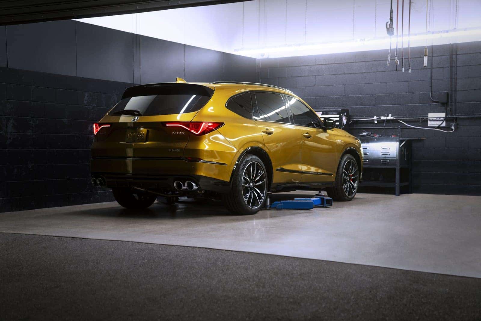An Acura MDX Type S seen from the rear three-quarter view in a service bay, raised slightly on a low-profile lift