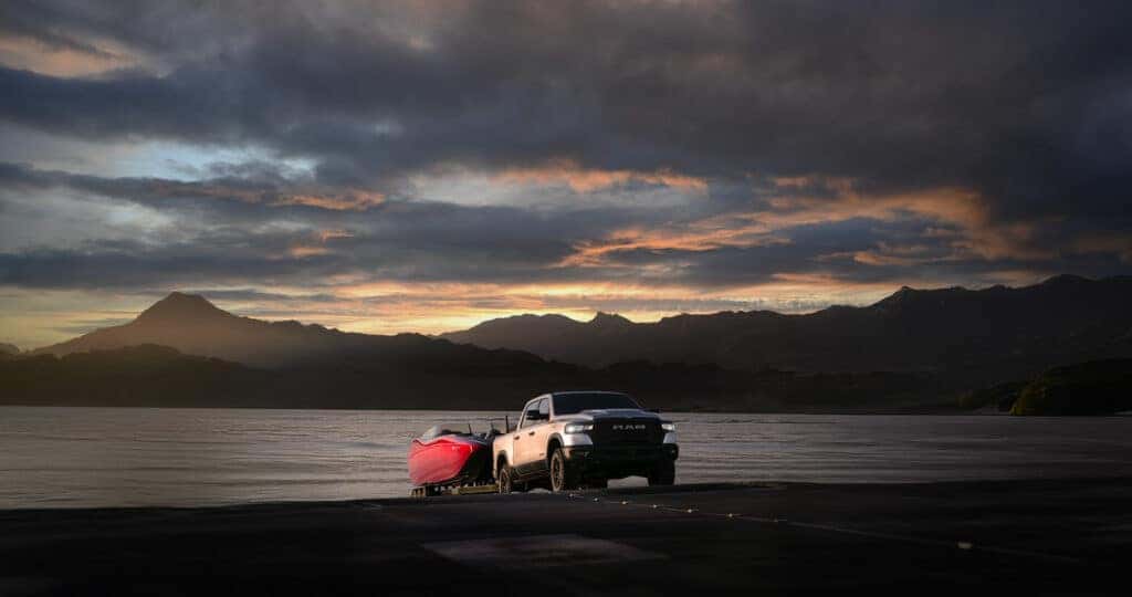 2025 Ram 1500 pulling a large boat out of a mountain lake at sunset