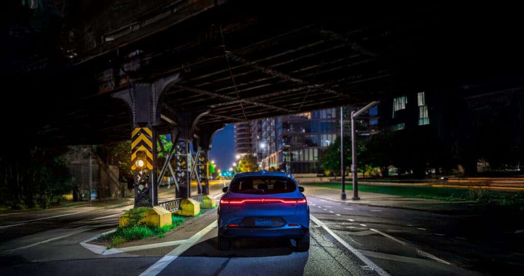 2025-Dodge-Hornet-parked-under-a-train-bridge-in-a-large-city-at-night-with-its-taillights-glowing