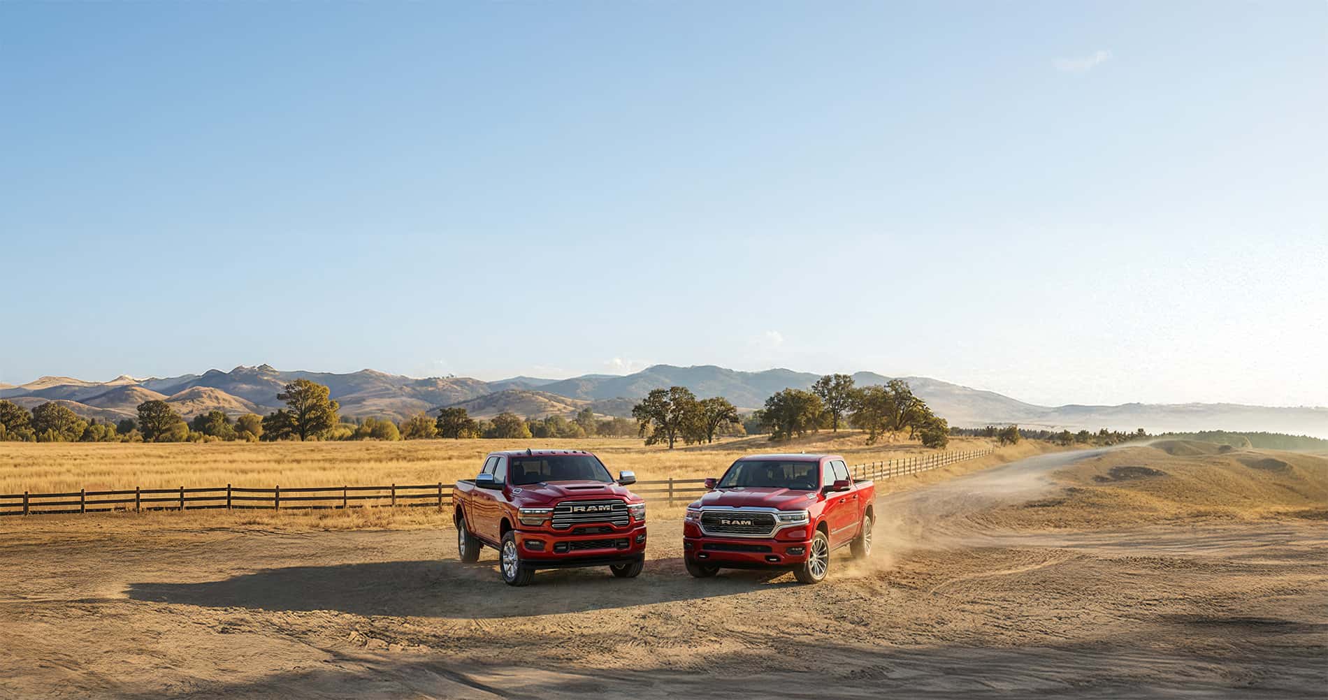 2026 Ram 1500 vs 2500 parked on a gravel road near a wooden fence with fields and mountain range in the distance