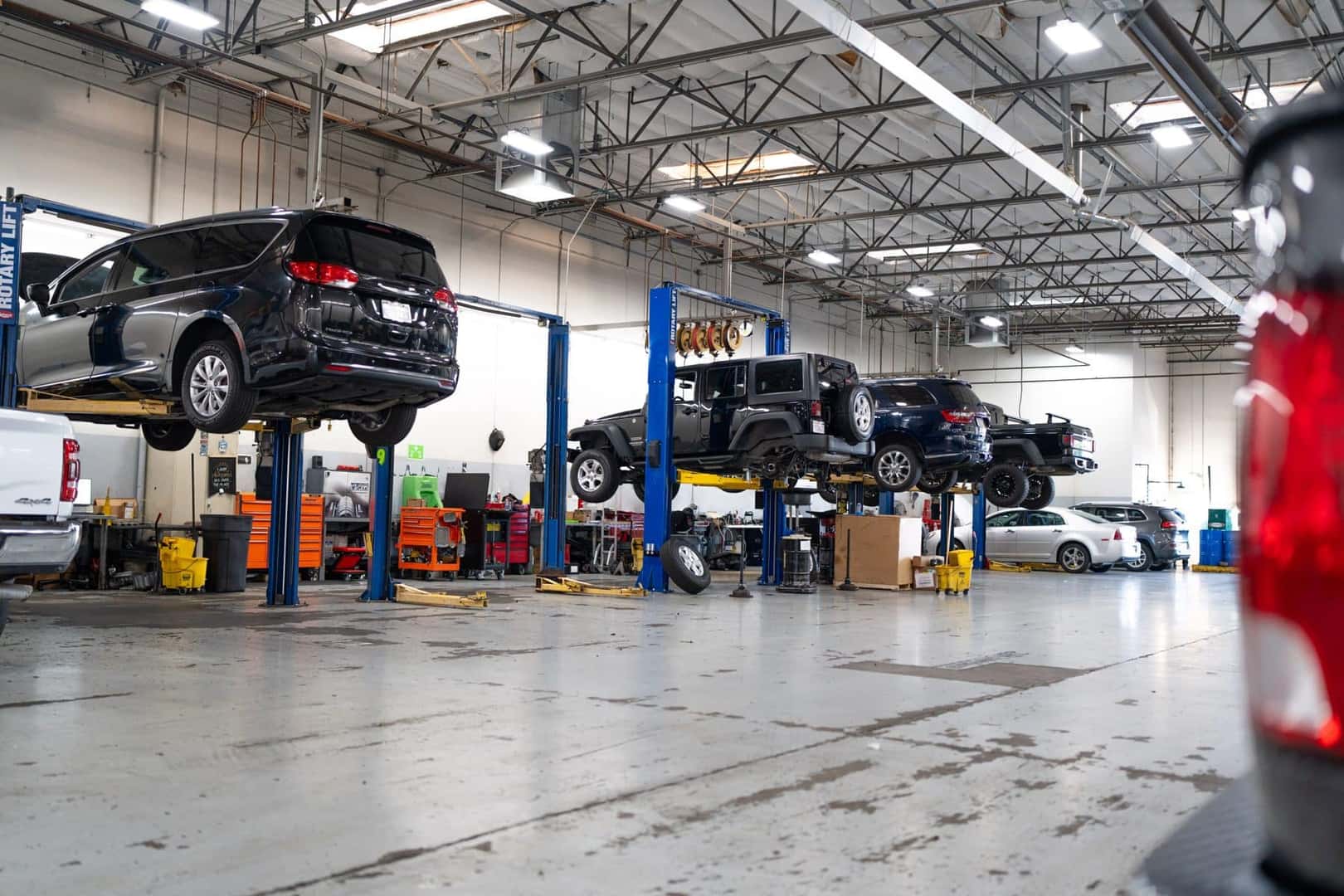 A Chrysler Pacifica, a Jeep Wrangler and other vehicles raised on lifts in the Elk Grove Dodge Chrysler Jeep Ram service shop