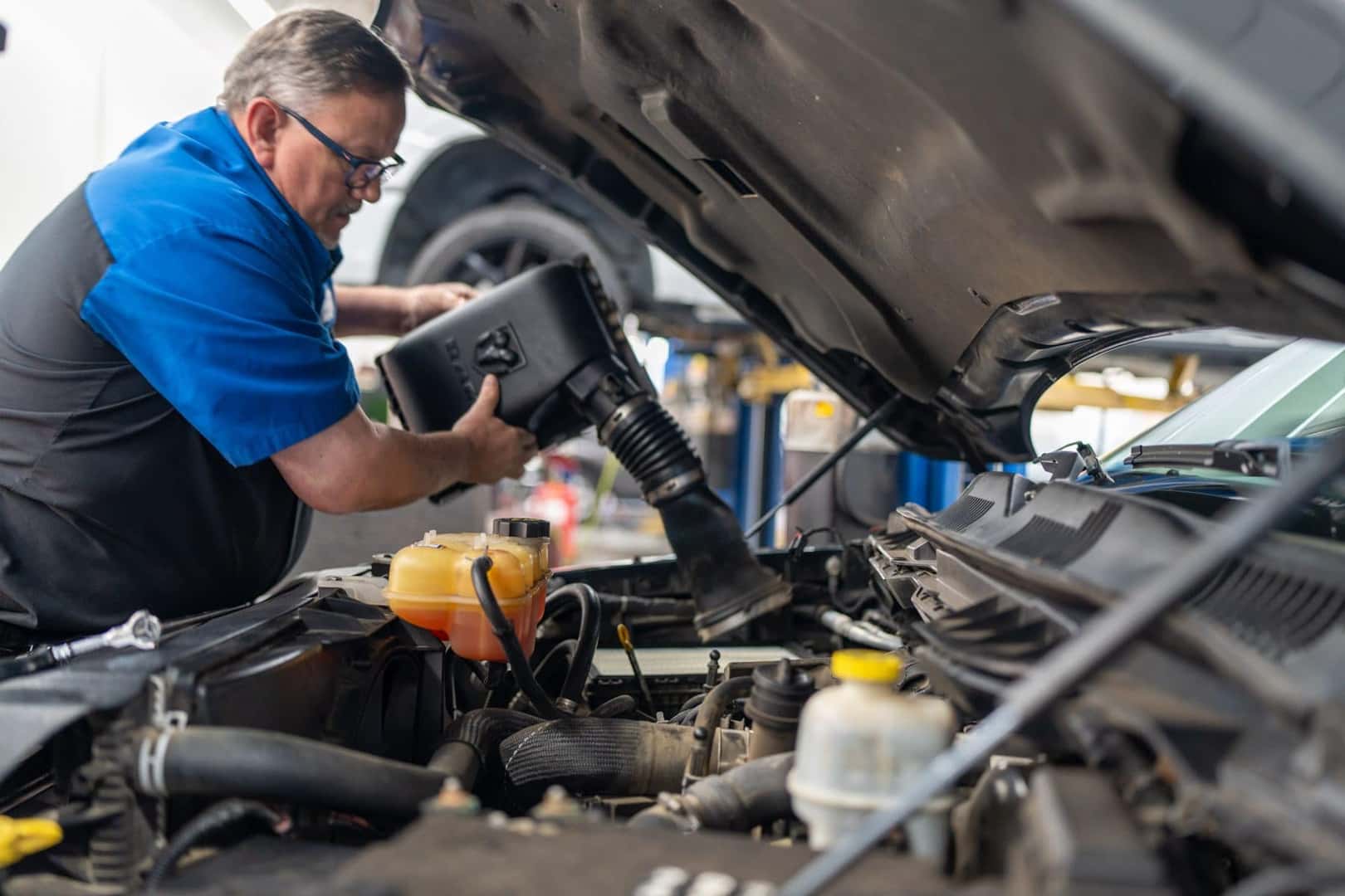 A technician in the Elk Grove Dodge Chrysler Jeep Ram service shop lifting the air intake housing from an engine under an open hood