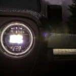 The round headlight of a 2018 Jeep Wrangler is shown at night and is popular among used Jeeps for sale in Ennis, TX.