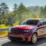 A red 2019 Jeep Grand Cherokee is shown driving down a highway with trees and mountains in the background near a Jeep dealership in Dalles, TX.