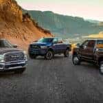 Three 2019 RAM 2500 trucks are parked on a desert road with hills.