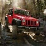 A red 2016 used Jeep Wrangler for sale is on a rocky trail outside Ennis, TX.