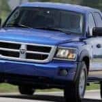 A blue 2011 Dodge Dakota is driving on a grass lined road near Ennis, TX.