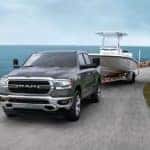A gray 2020 Ram 1500 is towing a boat next to a lake.