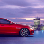 Red Jaguar XE parked on roof of city building with skyline at dusk in background