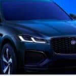 A dark green 2026 Jaguar F-Pace SUV with a prominent black mesh front grille and sleek LED headlights is showcased in a studio setting against a vibrant blue background.