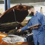 Certified Hyundai service technician using a diagnostic tablet while performing an open recall inspection under the hood