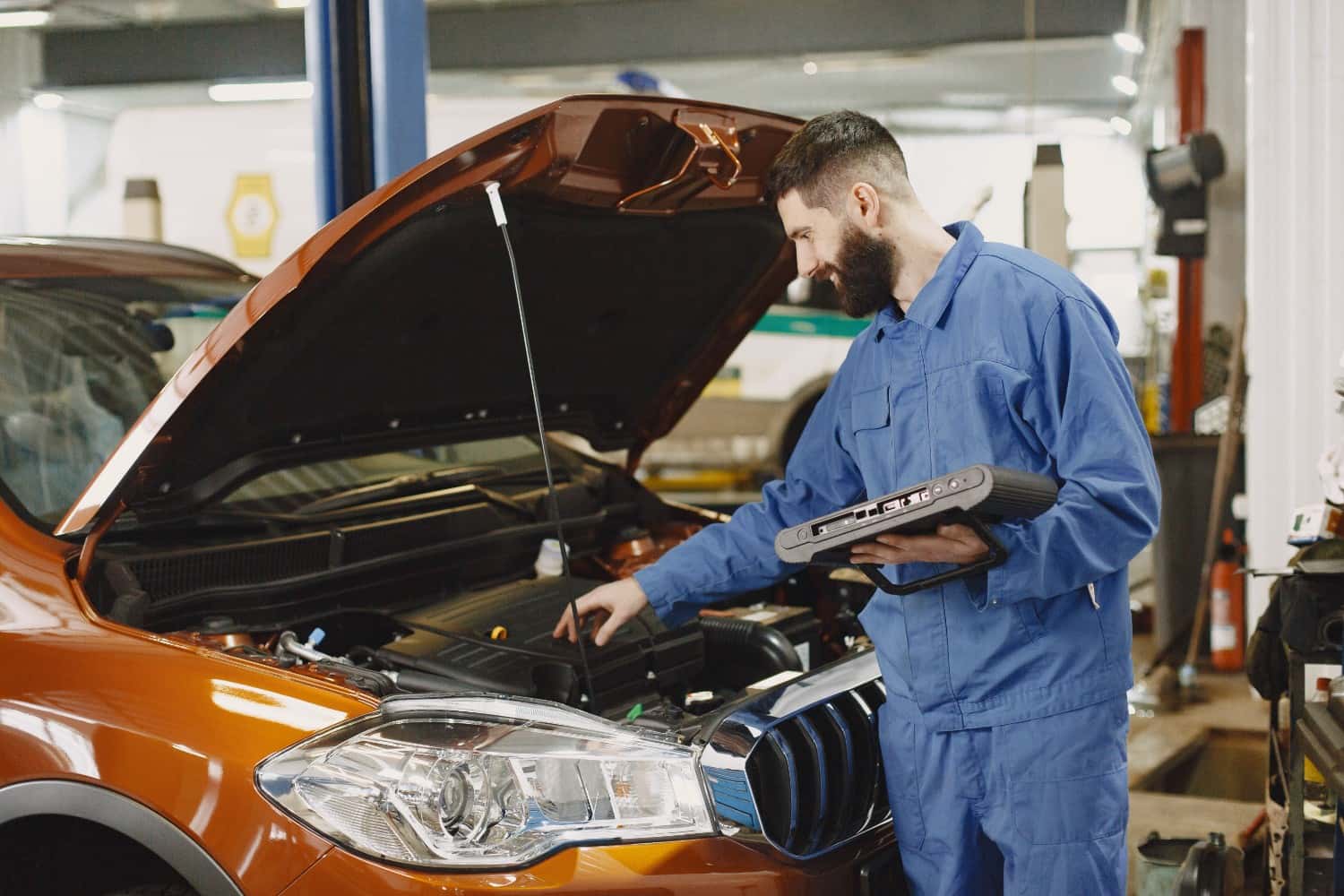 Certified Hyundai service technician using a diagnostic tablet while performing an open recall inspection under the hood
