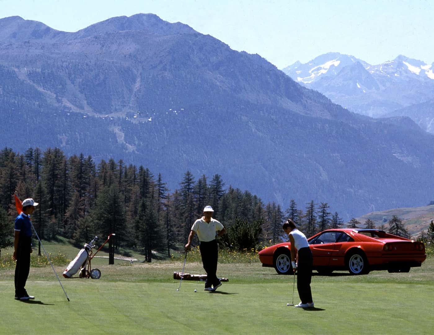 Three people golfing with a classic Ferrari in the background