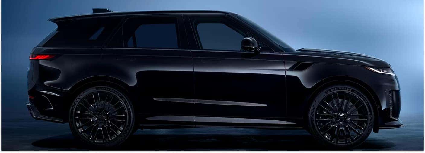 A side profile view of a black 2026 Range Rover Sport with matching black multi-spoke wheels, set against a dark blue studio background.