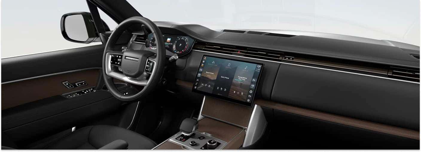 Front cabin interior of the 2026 Range Rover featuring the steering wheel, center touchscreen, and brown wood trim.