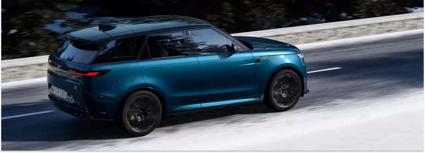 Rear three-quarter view of a teal 2026 Range Rover Sport driving on a snowy road.