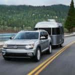 Silver 2018 Volkswagen Atlas towing trailer on highway with forested hills in background