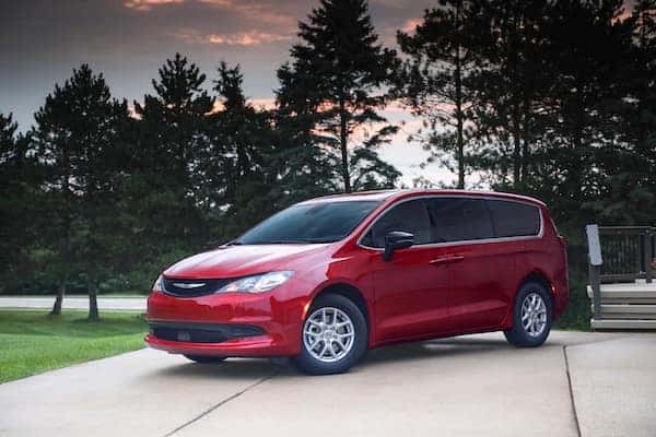 Red Chrysler Voyager parked in front of trees on driveway.