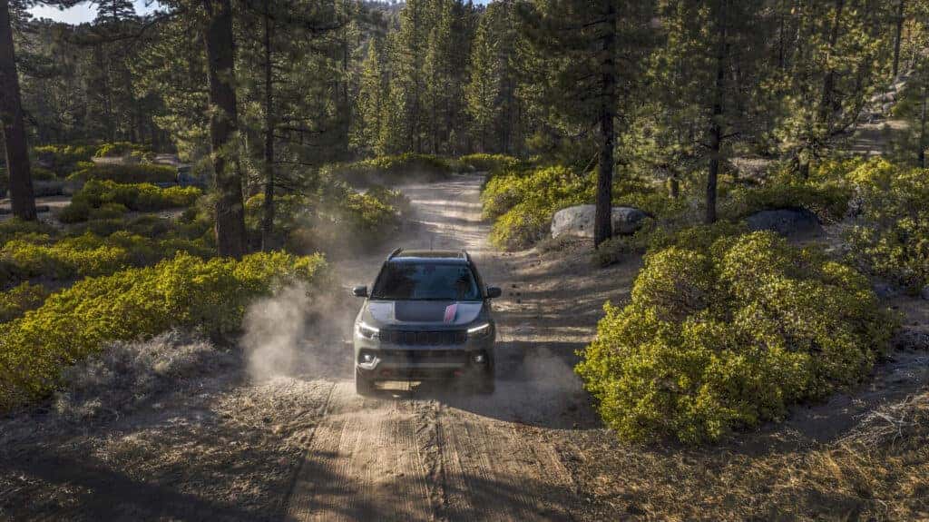 2025 Jeep Compass exploring an off-road trail, trees on both sides.