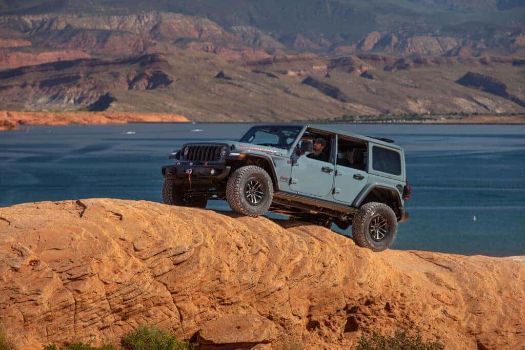 A 2025 Jeep Wrangler Rubicon traversing rocks next to a body of water.