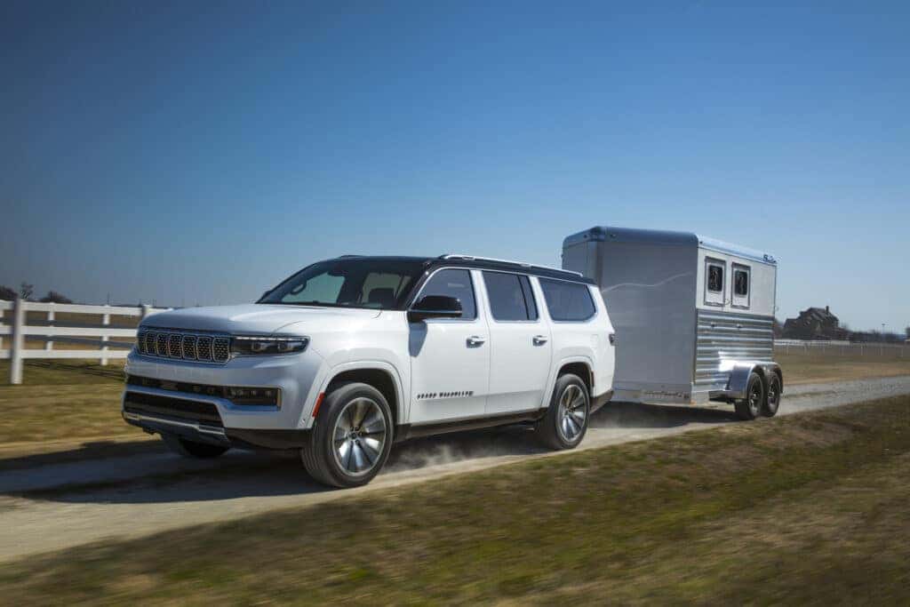 A white 2025 Jeep Grand Wagoneer pulls a trailer behind it.