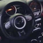 Photo of the inside of a MINI Cooper, focused on the steering wheel and brand emblem.