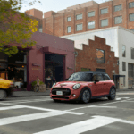 Coral Red MINI Cooper 2 Door on a busy cobble street road.