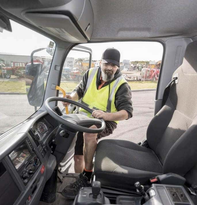 Interior shot of a man in a hi-viz vest entering through the driver door of an Isuzu truck.