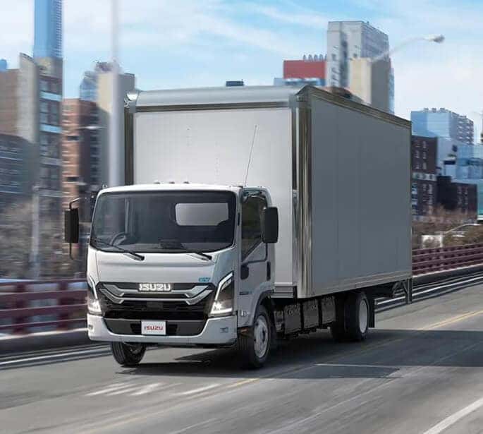 Exterior front three-quarter view of a white Isuzu truck driving down a city highway.