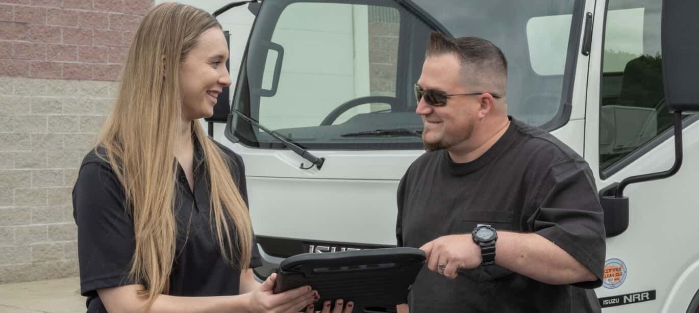 An Isuzu parts and service representative holds a table while a driver points to it and smiles.