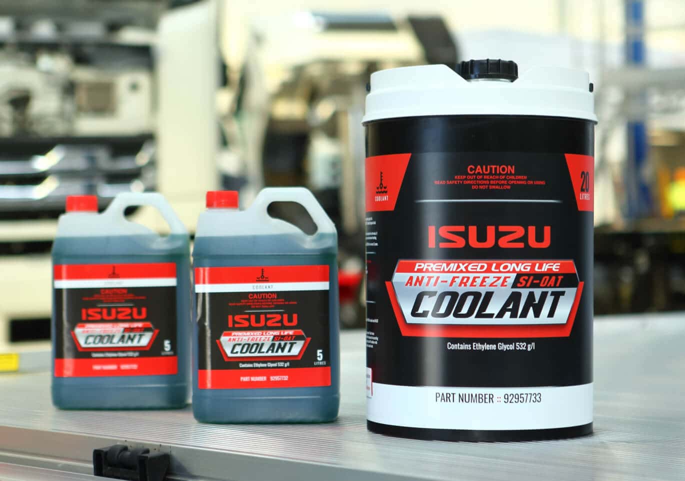 Three jugs of Isuzu OEM coolant sitting on a table inside a bright warehouse.