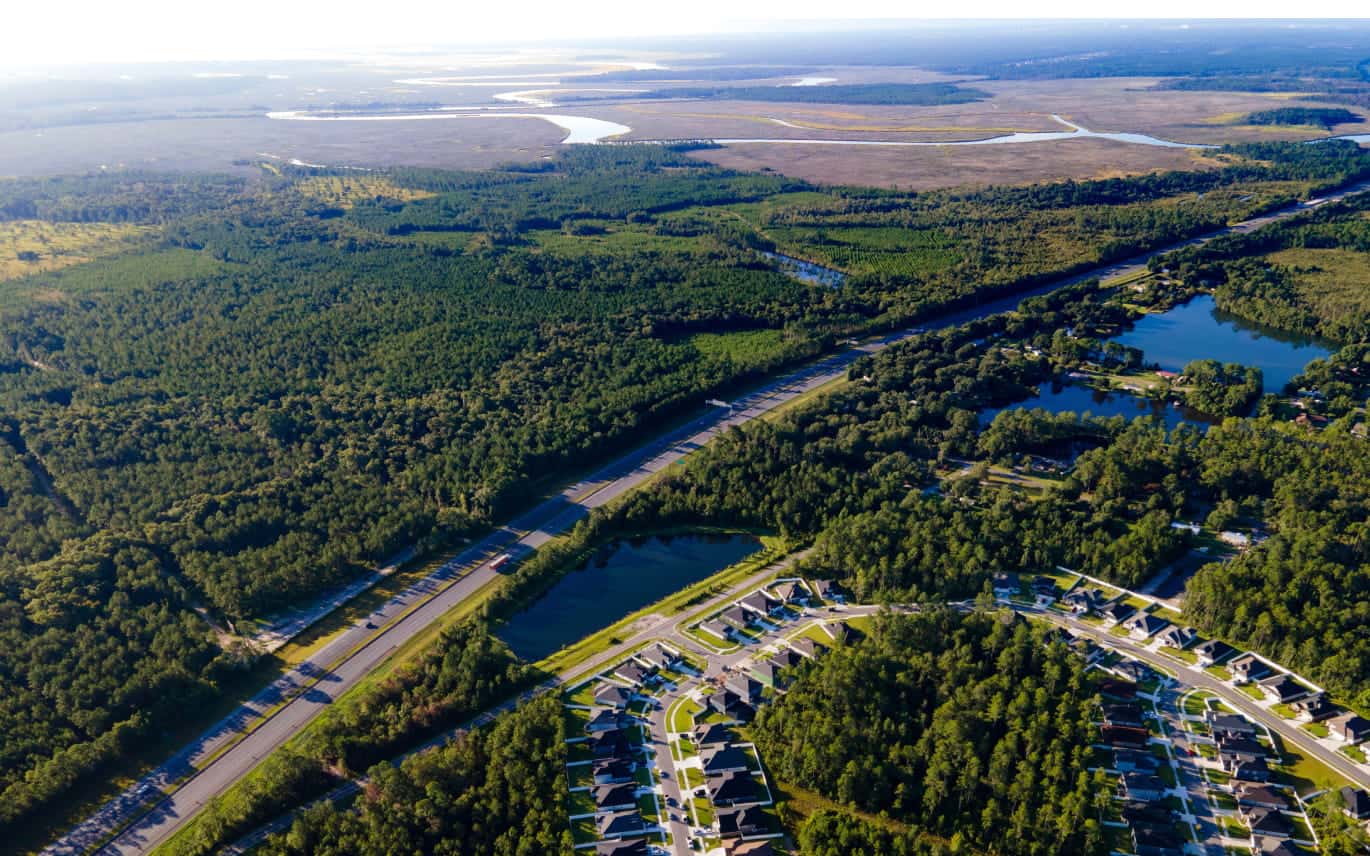 Aerial view of a residential area surrounded by dense forest, ponds, and winding waterways.