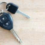 Two black car keys on a silver loop, sitting on a light brown table